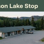 A roadside motel and SUV near evergreen forest and hills in Watson Lake.