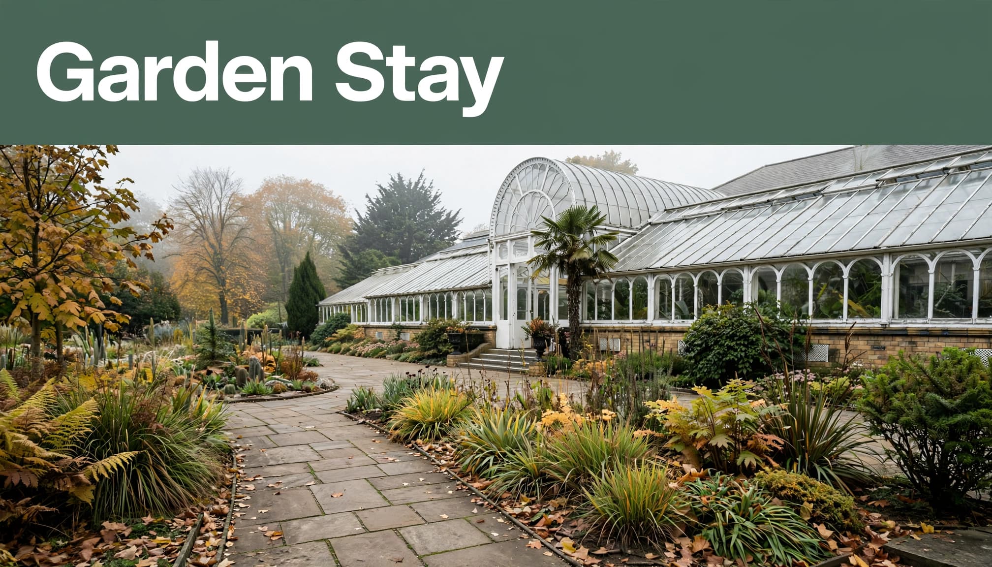 A glasshouse and garden path surrounded by mature greenery at Birmingham Botanical Gardens.