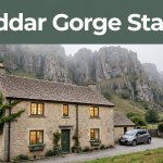 A stone guesthouse with warm windows and Cheddar Gorge cliffs behind it.