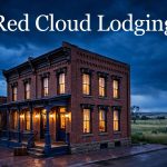 Historic Red Cloud lodging house with glowing windows, a suitcase, and prairie scenery at dusk.