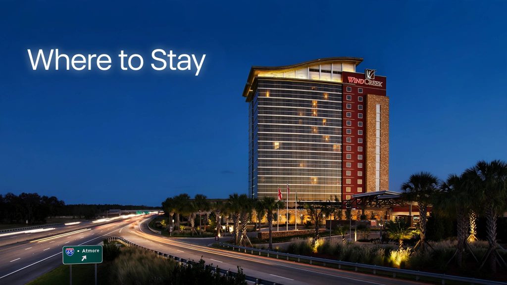 Wind Creek Casino and Hotel glowing at dusk with palm trees and a highway nearby.