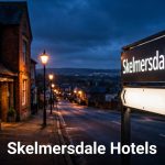 Lit Skelmersdale hotel sign beside a brick building at dusk.