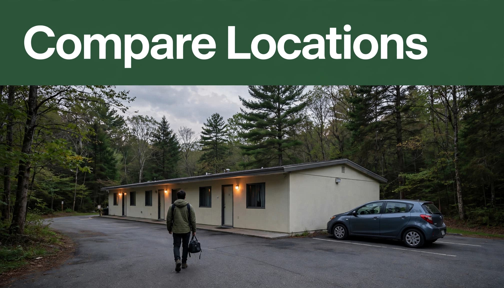 A traveler stands beside a compact car outside a wooded roadside motel at dusk.