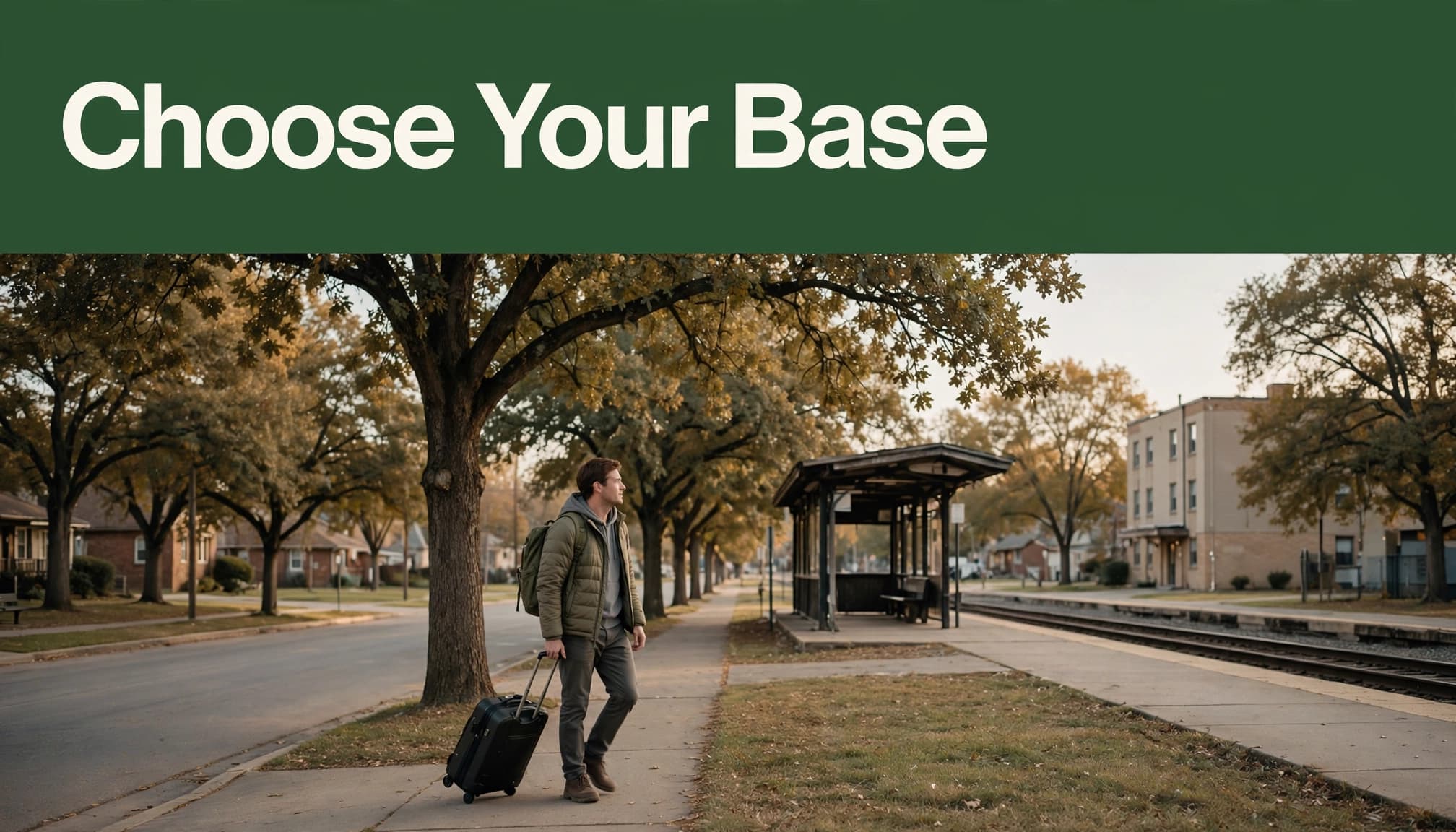 A traveler with one suitcase walks toward a small train platform near a suburban hotel.